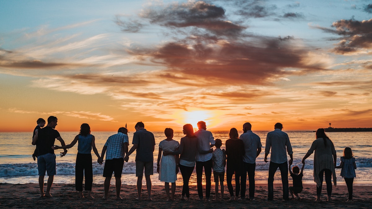A multi-generational family holding hands on a beach at sunset — representing family support and togetherness