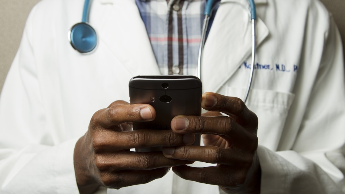 A doctor in a white coat holding a smartphone, representing a care team call with a patient managing health at home